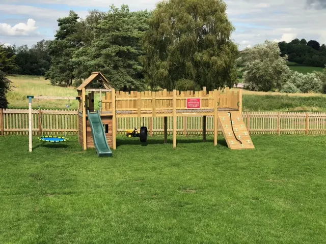 The children's outdoor play area with a climbing frame and slide, overlooking fields